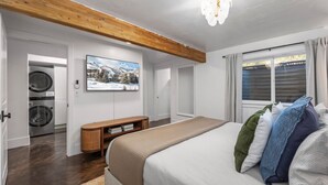 Un dormitorio con cama, televisión, lavadora y una viga de techo de madera.