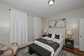A bedroom with a bed, bedside tables, a bench, a chair, and two wall-mounted lamps.