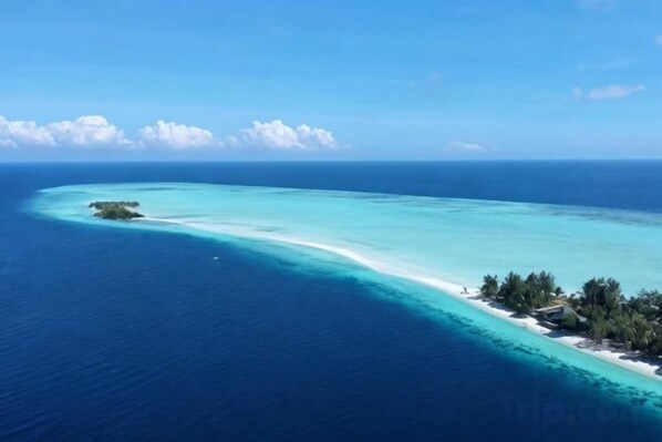 Una isla tropical con un mar turquesa cristalino, una playa arenosa y un pequeño conjunto de edificios.