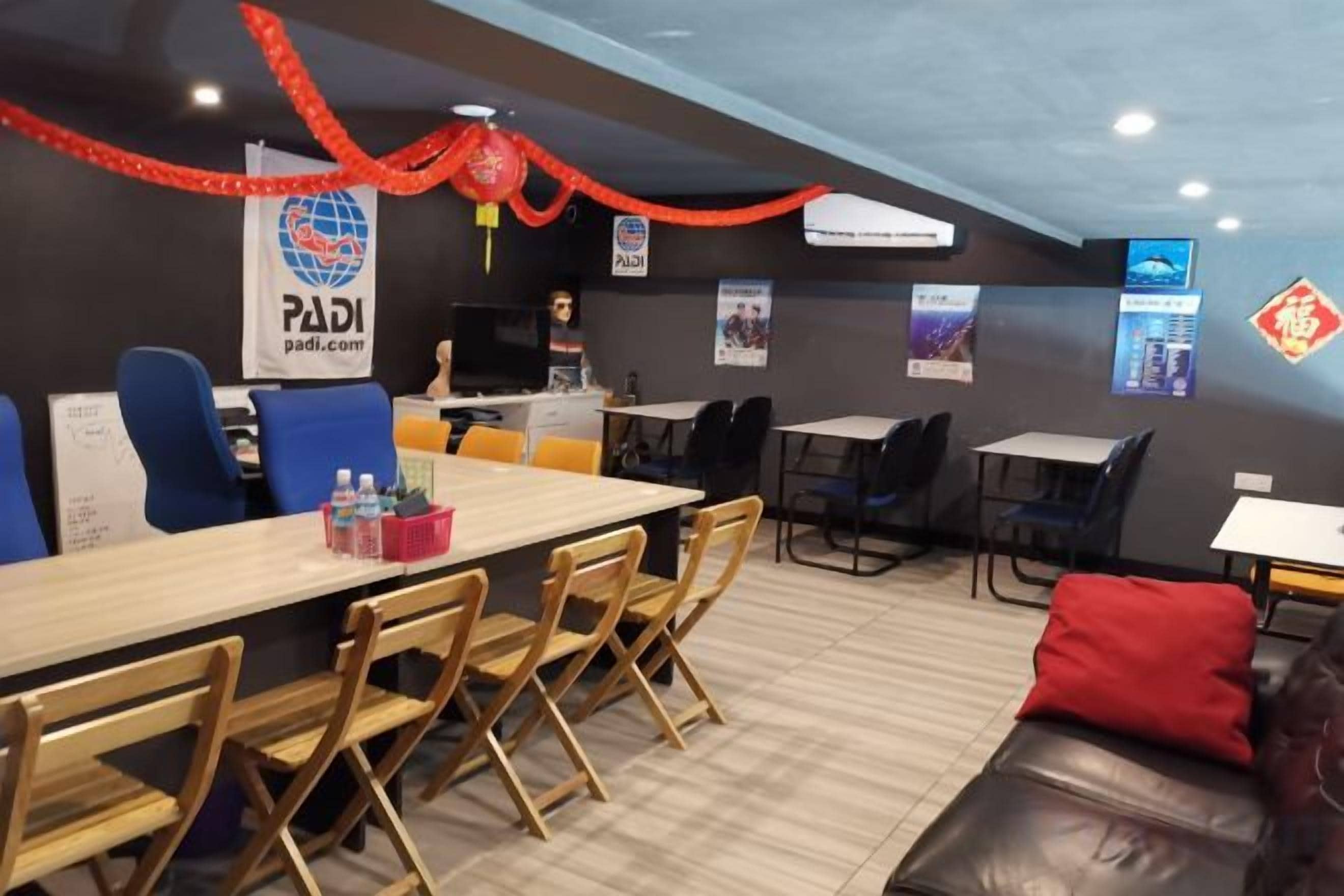 A modern lounge area with a long wooden table, blue and black chairs, a red couch, and a TV screen.