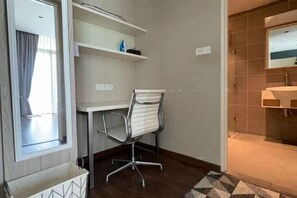 A hotel room with a desk, chair, and a bathroom with a sink and mirror.