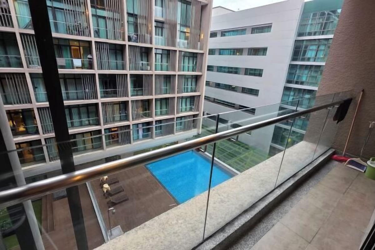 A modern building with a glass balcony overlooking a swimming pool and a courtyard.