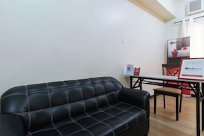 A black leather sofa, a small table, and a chair in a room with white walls and a wooden floor.