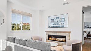 A modern living room with a grey sofa, a stone fireplace, and a framed cityscape poster on the wall. - 2 bedroom - WiFi, AC, garaged off-street parking with EV Charger. (Solvang)