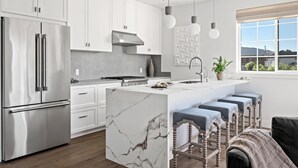 A modern kitchen with white cabinets, a stainless steel refrigerator, a marble island, and bar stools. - 2 bedroom - WiFi, AC, garaged off-street parking with EV Charger. (Solvang)