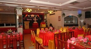A banquet hall with round tables, red and gold chairs, and a stage with a backdrop.