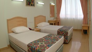 Hotellihuone, jossa on kaksi sänkyä, työpöytä, tuoli, peili ja ikkuna, jossa on verhot.