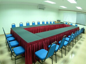 A conference room with a long table, blue chairs, a whiteboard, and an air conditioning unit.