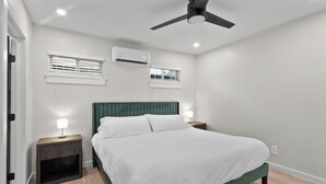 Ein Schlafzimmer mit einem Bett, zwei Nachttischen, einem Deckenventilator und zwei Wand-Klimaanlagen.