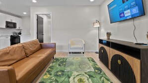Ein modernes Wohnzimmer mit einer Ledersofa, einem Glastisch, einem flachbildfernseher an der Wand und einem minimalistischen Einrichtungsstil.