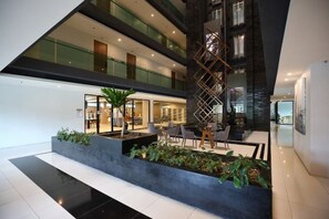 Eine moderne Hotellobby mit einer zentralen Sitzgruppe, einer Treppe und einem Glasgeländer.
