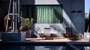A pool area with a modern chair, a sculpture, and a large window with curtains.