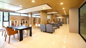 A spacious indoor area with a long table, several chairs, sofas, and bookshelves.