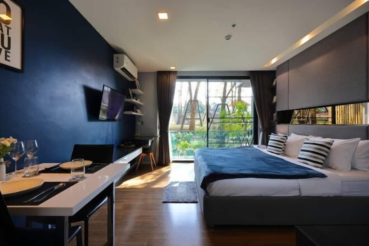Une chambre d’hôtel moderne dotée d’un grand lit, d’un bureau avec une chaise, d’une télévision et offrant une vue sur la verdure environnante.