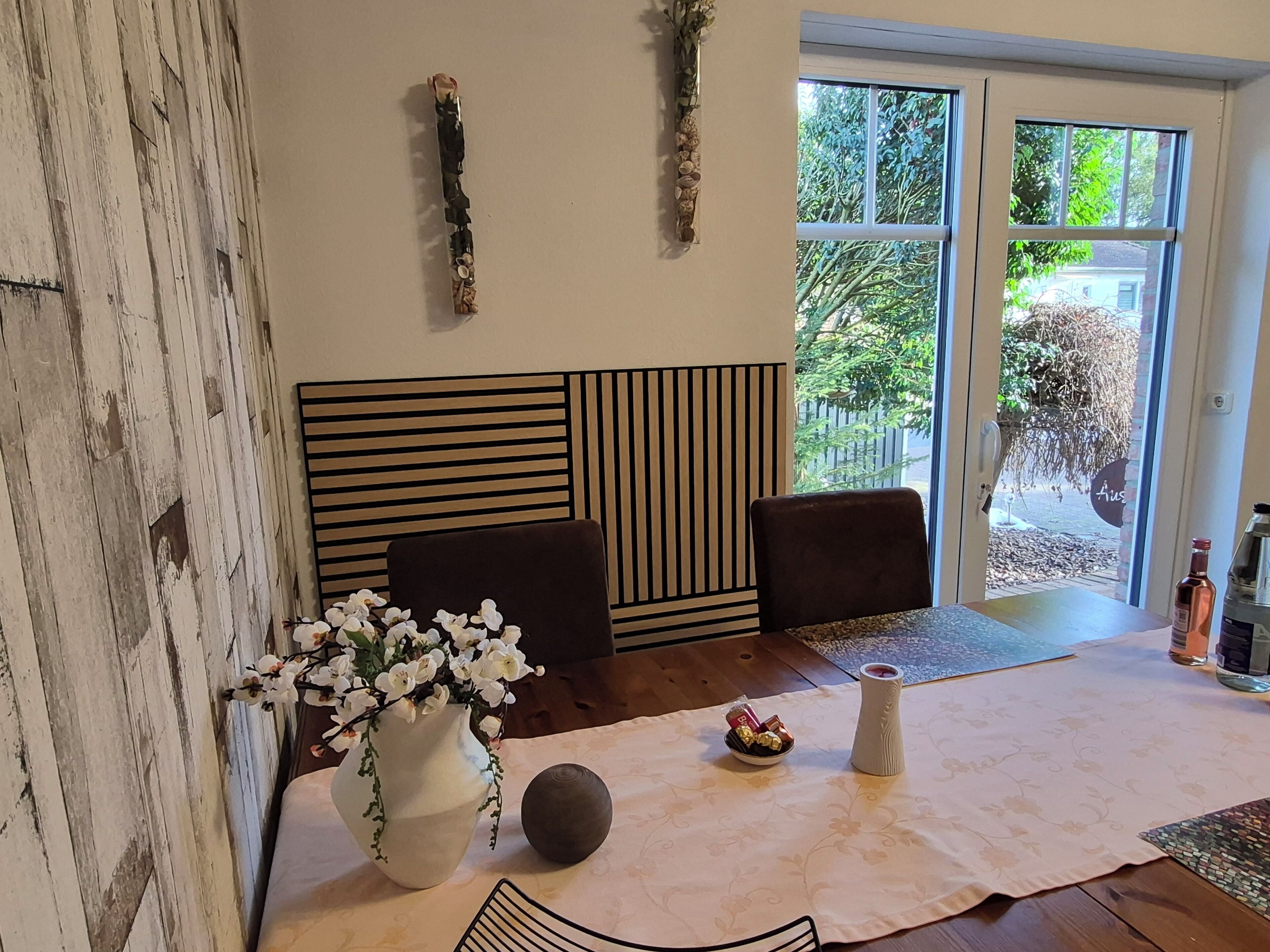 A room with a wooden wall, a sofa, a table with a vase of flowers, a bowl of chocolates, and a bottle.