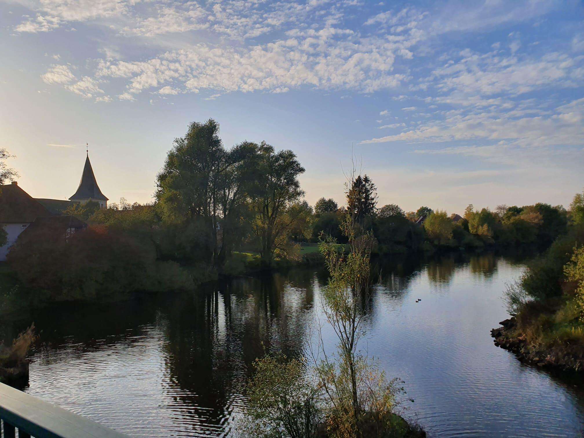 A calm river with trees and a church in the background.