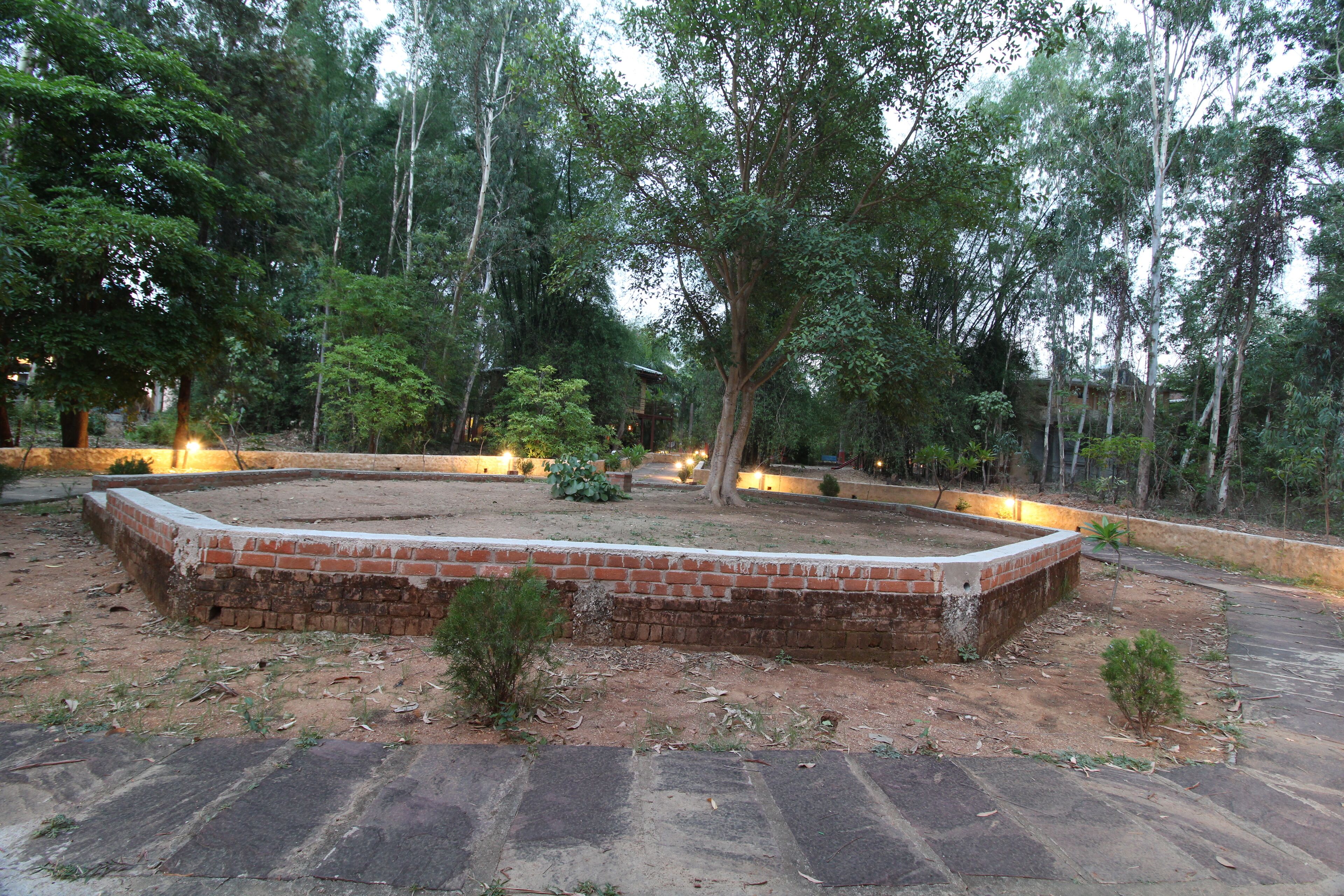 Un jardín ajardinado con un macetero de ladrillo, árboles y una zona pavimentada.