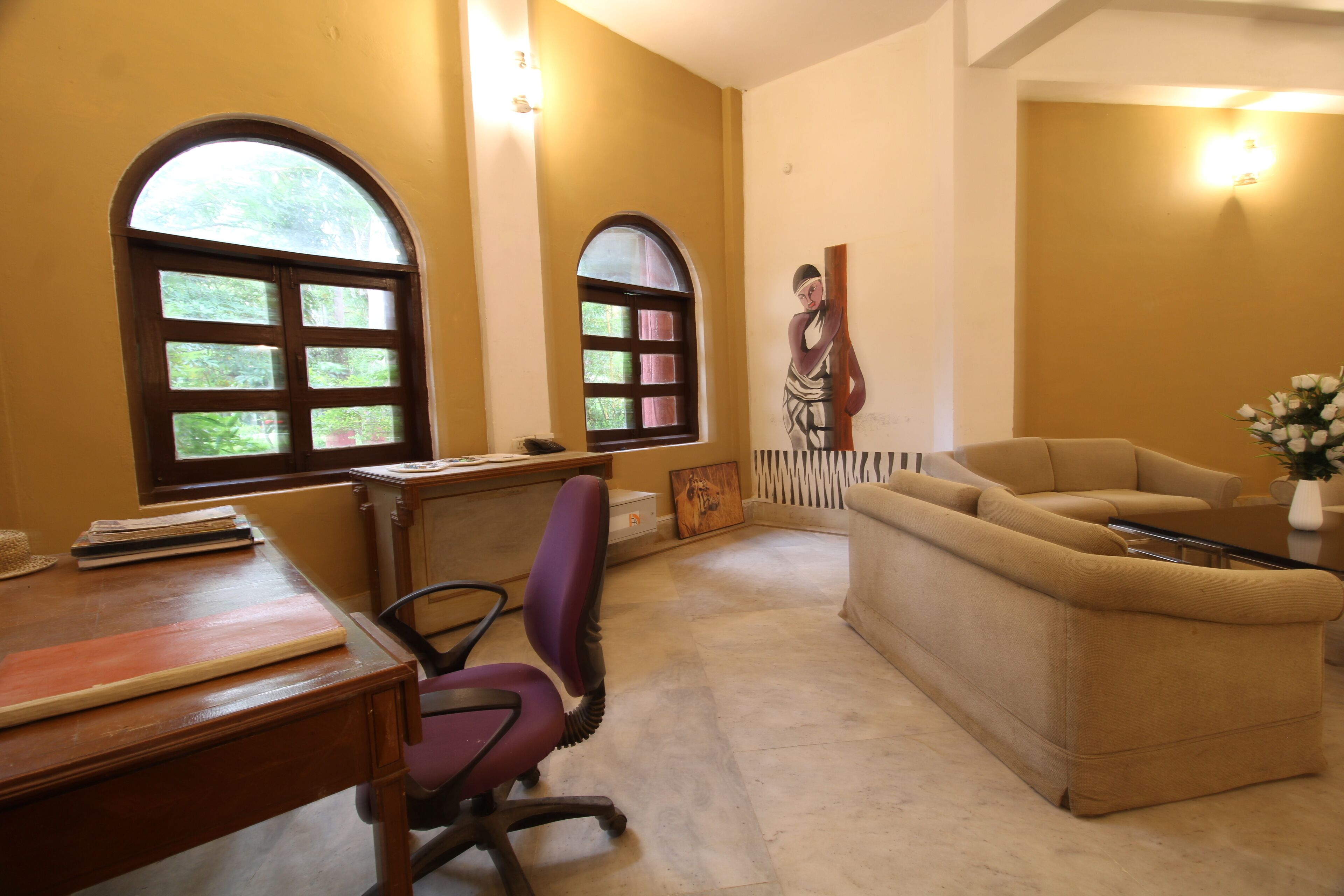 Una habitación con dos ventanas de arco, un escritorio con una silla, un sofá y una estatua decorativa.