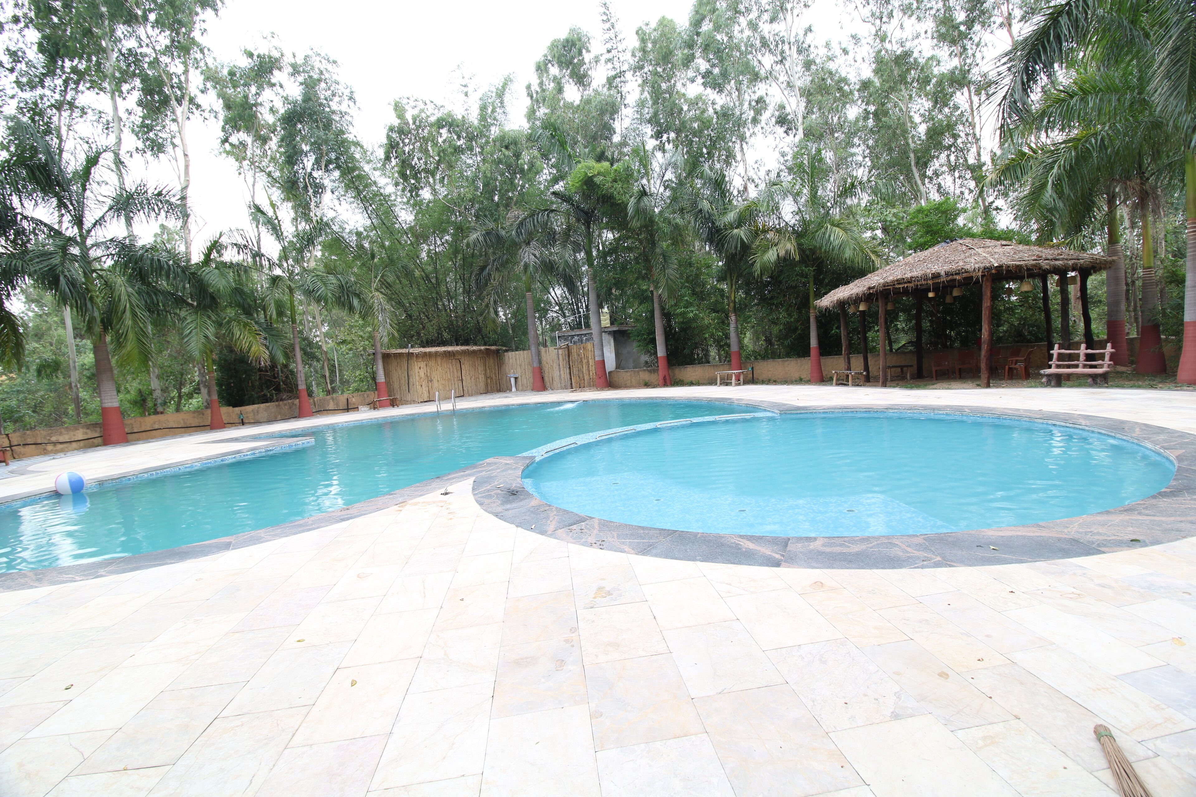 A swimming pool with a circular edge, surrounded by a tiled deck and a wooden gazebo.