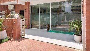 A modern building with a glass entrance, a brick exterior, and a green mat at the entrance. - Saffron Inn  (Greater Noida)