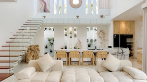 Een moderne woonkamer met een royale hoekbank, een houten eettafel en een glazen trap.