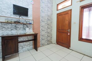 A room with a marble wall, a TV mounted above a wooden desk, a stone-patterned wall, a wooden door, and a window with curtains. - ARBA Artana & Chipsari Hotel Pangalengan (Pangalengan)
