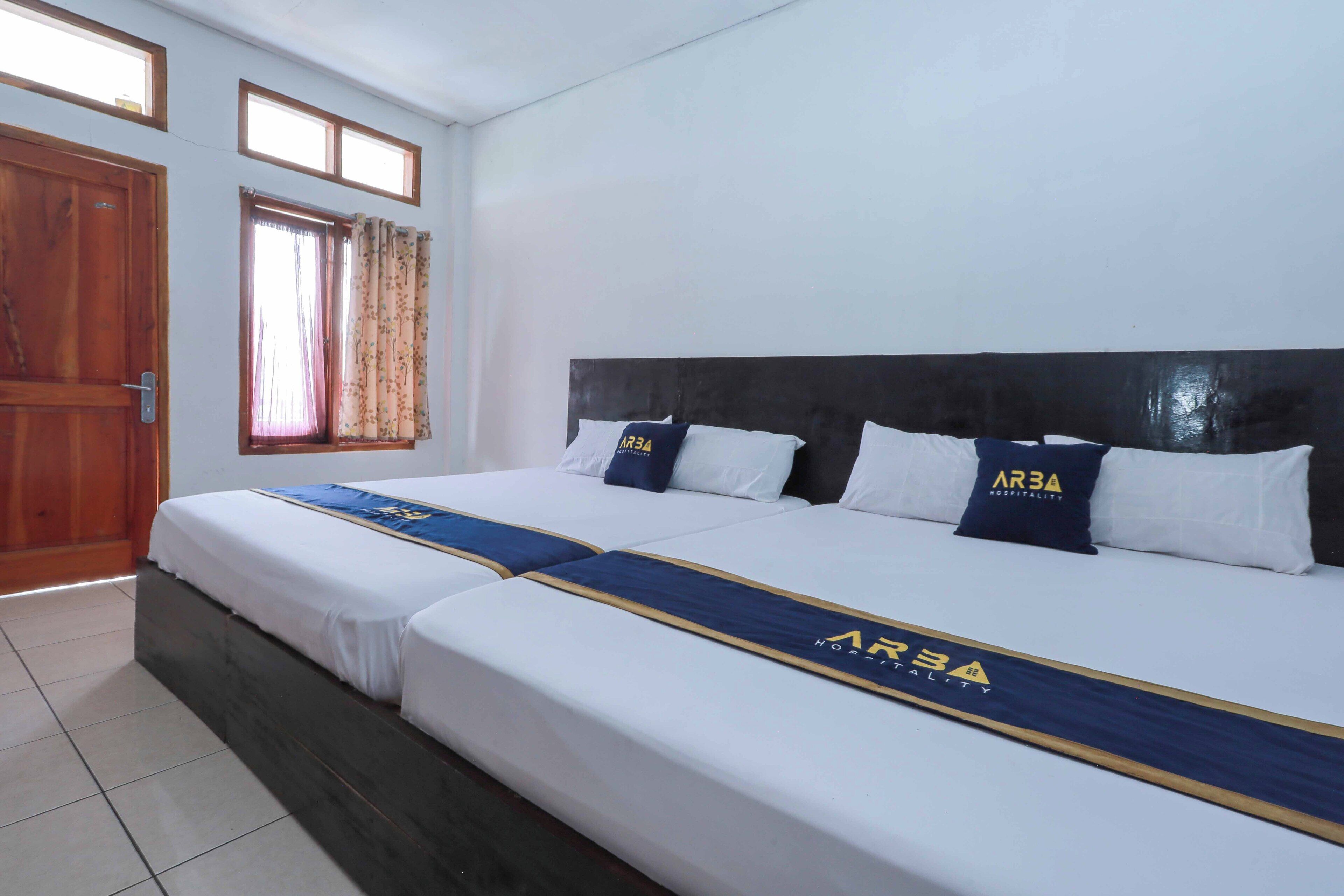 A hotel room with a large bed, two pillows with the hotel logo, a window with curtains, and a wooden door.