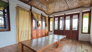 A room with a wooden table, large windows with curtains, and a thatched roof. - ARBA Artana & Chipsari Hotel Pangalengan (Pangalengan)