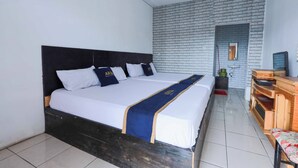A hotel room with a large bed, a wooden dresser, a television, and a brick wall. - ARBA Artana & Chipsari Hotel Pangalengan (Pangalengan)