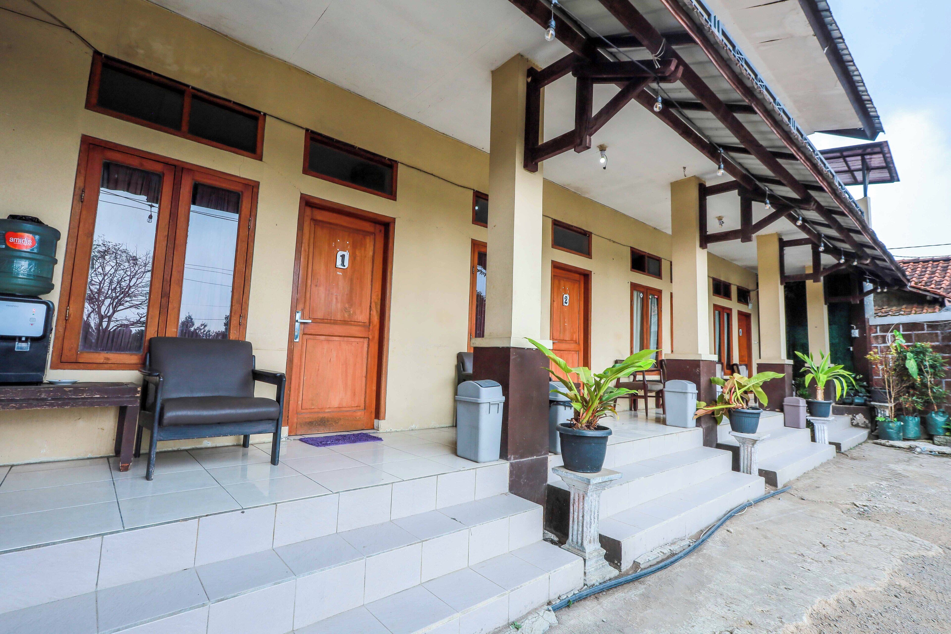 A building with a tiled entrance, wooden doors, and a covered porch area with potted plants.