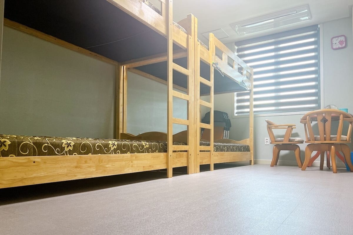 A bunk bed with a ladder, a small table with chairs, and a window with blinds.