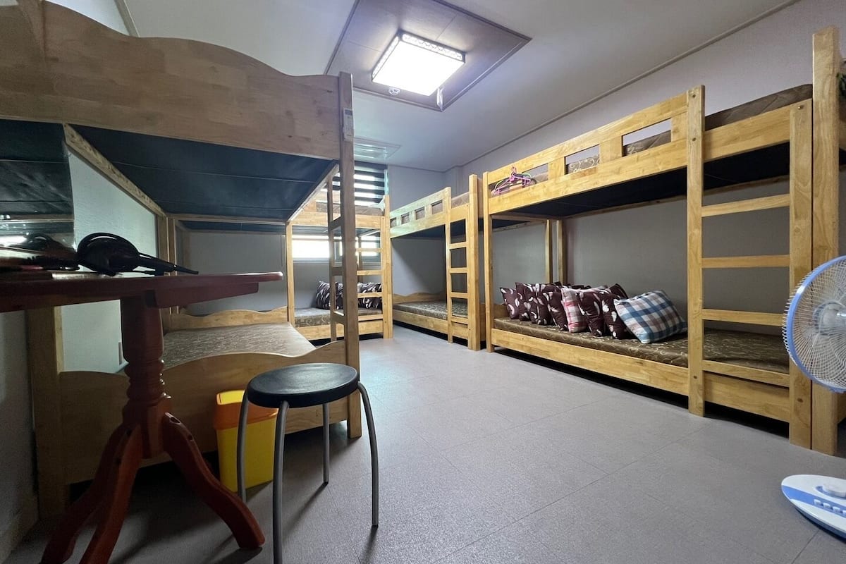 A room with bunk beds, a desk, a chair, and a fan.