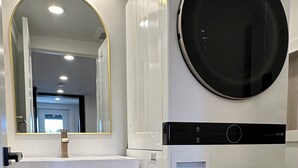 A modern bathroom with a double washing machine, a wooden cabinet, and a mirror. - Charming Madrona Stay • Walk to Lake & Cafes, Shops, A/C • Parking (Seattle)