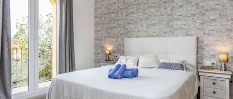 A bedroom with a brick-patterned wall, a large bed with a white headboard, two bedside tables with lamps, and a view through a glass door.