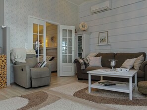 A living room with a sofa, armchair, and coffee table. There is a door leading to another room, a fireplace, and a wall-mounted air conditioner. - Rehviranta by Interhome (Kuopio)