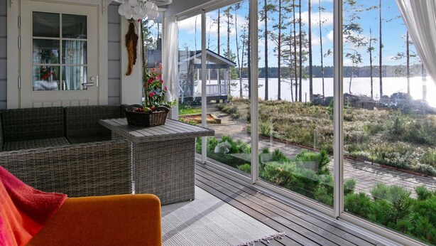 A sunlit room with a wicker sofa, a small table with a basket, and a view of a lake and trees.