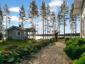A house with a paved pathway leading to a dock, surrounded by tall trees and a body of water. - Rehviranta by Interhome (Kuopio)