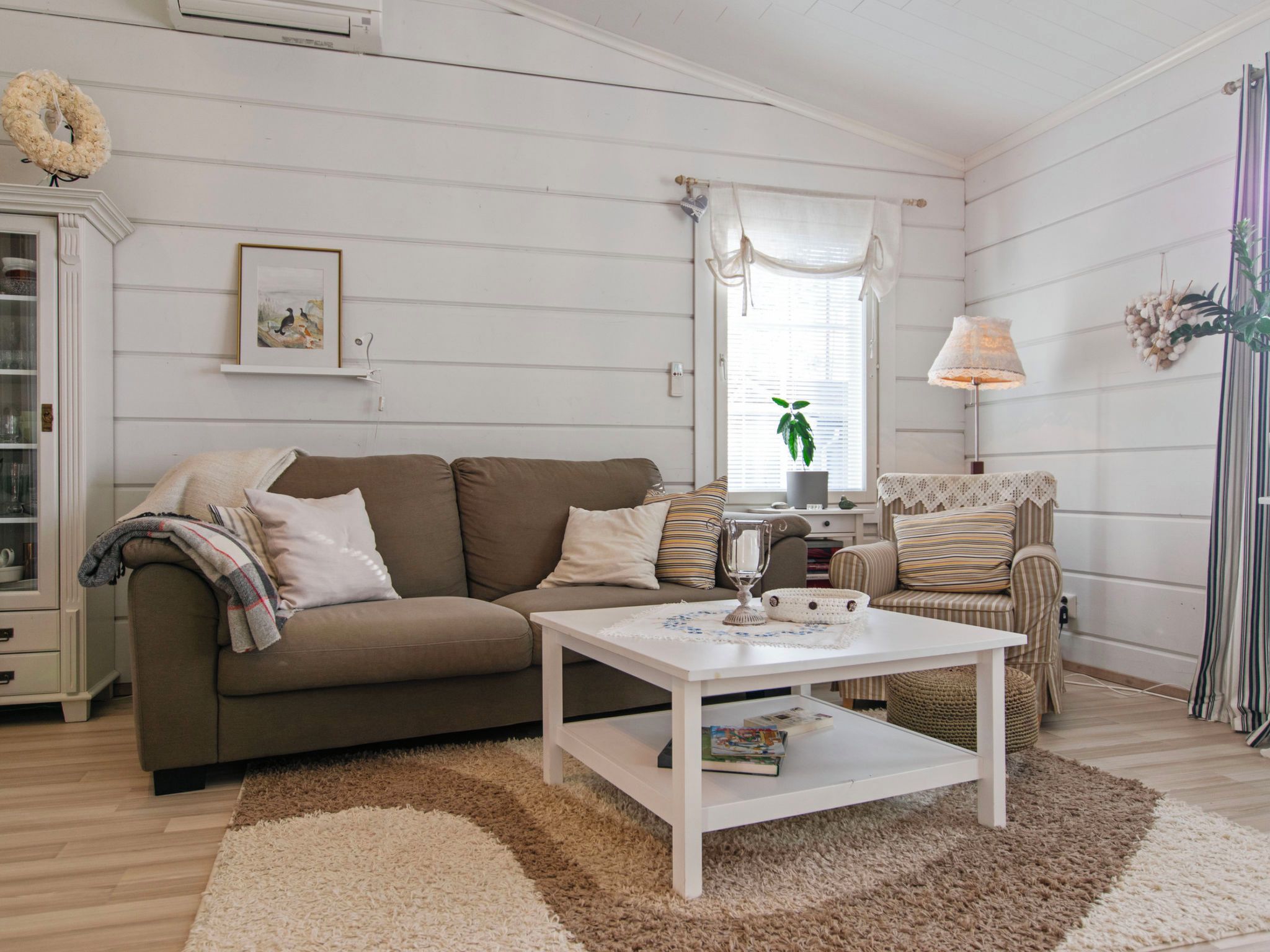 A cozy living room with a sofa, armchair, and coffee table, featuring a decorative wreath and a framed picture on the wall.