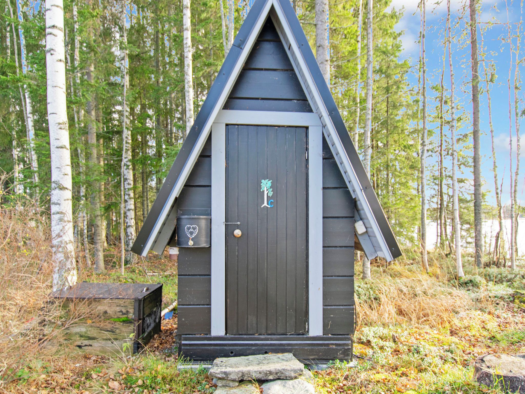 Une petite cabane en bois avec une porte sombre, une boîte aux lettres et une autre boîte aux lettres ornée d’un symbole en forme de cœur.