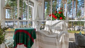 A cozy cabin with a wooden deck, a covered seating area, and a view of a lake and forest.