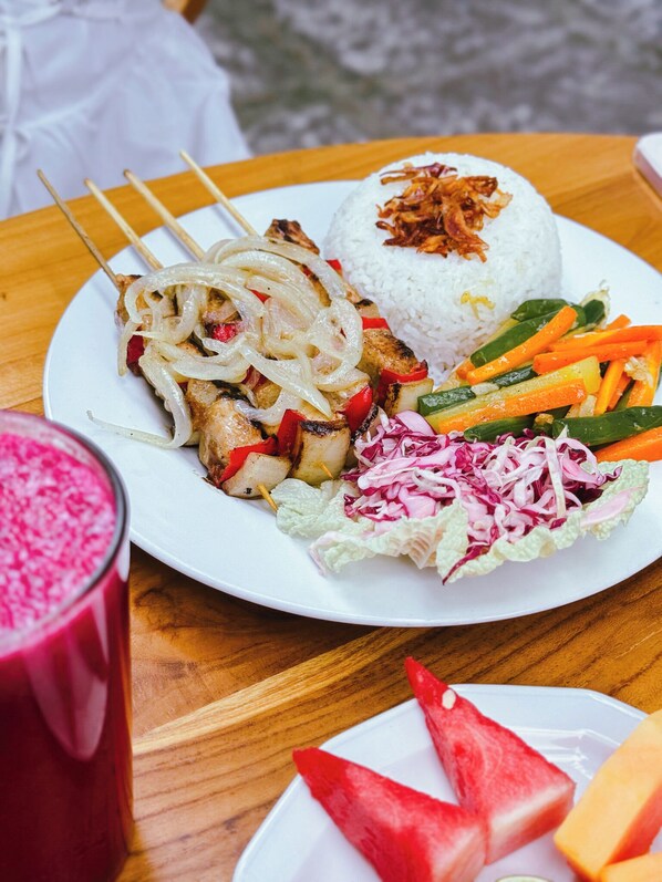 A plate of food with rice, grilled meat, vegetables, and a drink.
