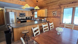 Interior de una cabaña de madera con cocina, comedor y un amplio ventanal.
