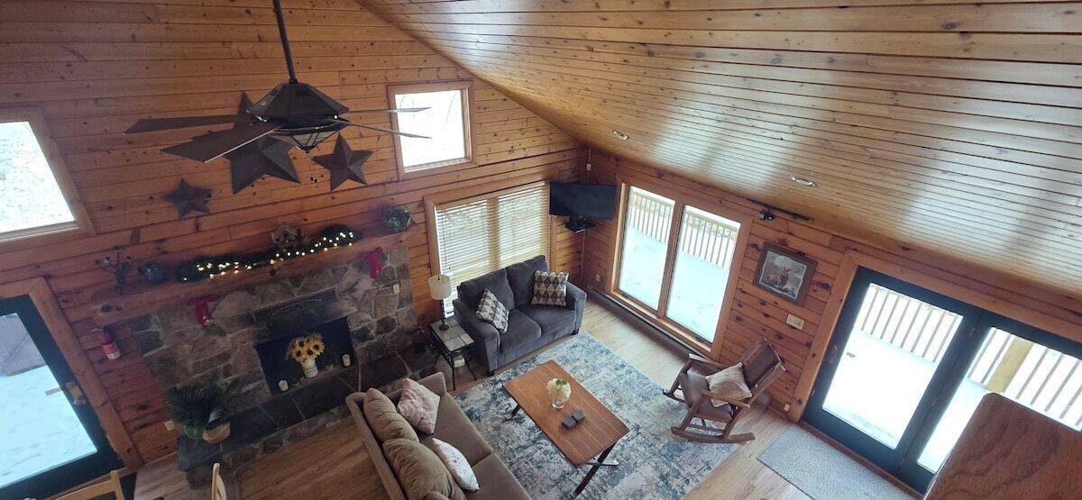 Un intérieur de chalet chaleureux avec une cheminée en pierre, un plafond en bois et de grandes fenêtres.