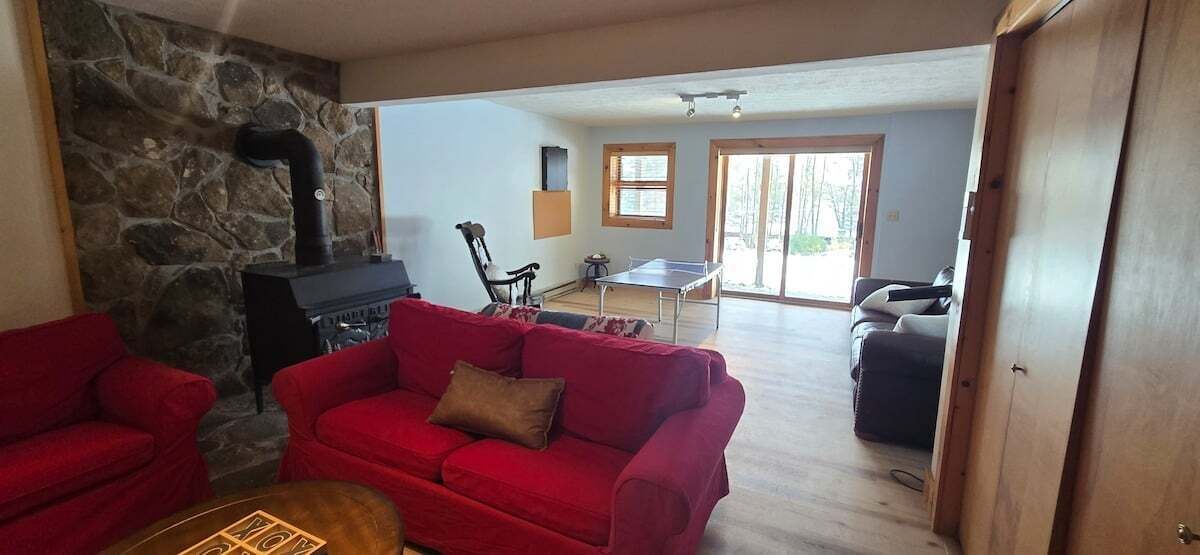 A cozy living room with a red sofa, a stone wall, a fireplace, and a dining area with a table and chairs.