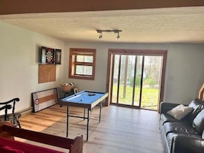 Una habitación con mesa de billar, sofá de cuero, dardo y ventana con vistas al exterior.