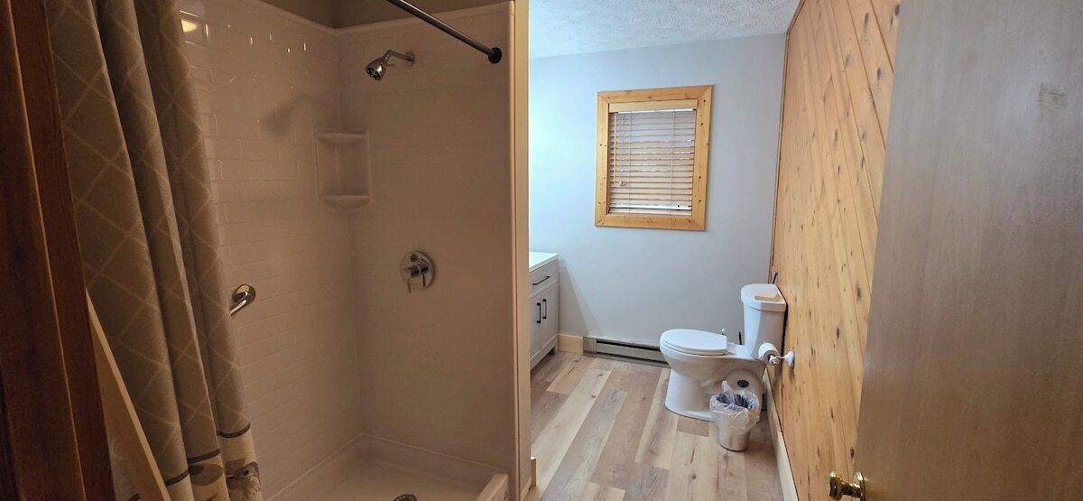 A bathroom with a shower, toilet, and a window.