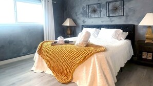 A modern bedroom with a large bed, two bedside lamps, a window with curtains, and a textured wall.