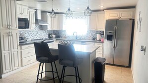 A modern kitchen with white cabinetry, a central island with bar stools, a stainless steel refrigerator, and pendant lighting.