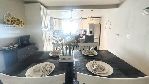A modern dining area with a dark countertop, white chairs, and a central vase with flowers.