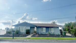 A single-story house with a gabled roof, a front porch, and a small front yard with plants.